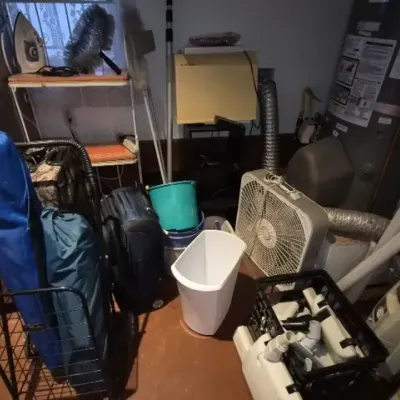 Sale Photo Thumbnail #156: Assorted household utility items and travel gear including a rolling shopping cart, folding chairs, luggage, a box fan, trash cans, and cleaning supplies.