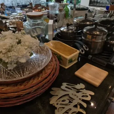 Sale Photo Thumbnail #125: Collection of kitchenware and home decor items including stainless steel cookware, woven charger plates, cut glass serving dishes, and a ceramic loaf pan.