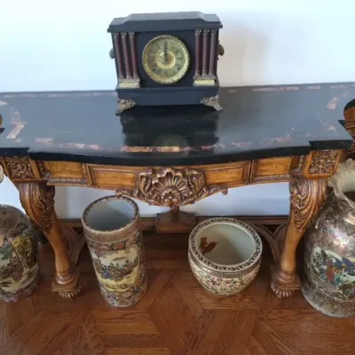Sale Photo Thumbnail #14: Ornate carved wood console table with a black inlaid top, topped with an antique mantel clock and framed by several large Asian-style porcelain vases and planters.