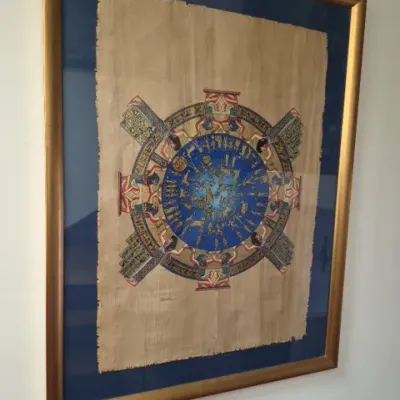 Sale Photo Thumbnail #73: Framed Egyptian papyrus painting depicting the Dendera zodiac calendar, mounted on a blue mat in a gold-finished frame.