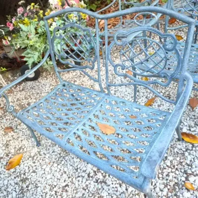 Sale Photo Thumbnail #174: Weathered blue-gray cast aluminum garden bench featuring an ornate lattice and medallion backrest design.