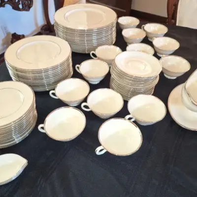 Sale Photo Thumbnail #117: Large white china dinnerware set with platinum rimming, including stacks of plates, saucers, teacups, and a gravy boat with an underplate.