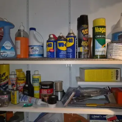 Sale Photo Thumbnail #167: Assortment of vintage and modern household chemical sprays, cleaning products, and maintenance supplies displayed on garage shelving.