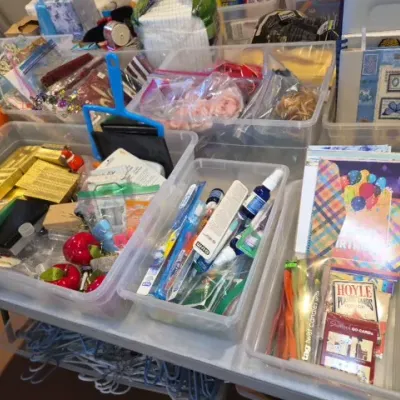 Sale Photo Thumbnail #162: Clear plastic storage bins filled with miscellaneous household items, craft supplies, toiletries, greeting cards, and playing cards.