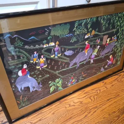 Sale Photo Thumbnail #71: Large framed embroidery artwork depicting a rural Asian agricultural scene with farmers and water buffalo, presented under glass in a black composite frame.
