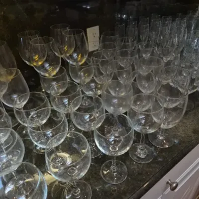 Sale Photo Thumbnail #127: Large collection of assorted clear glassware, including stemware, wine glasses, and tumblers, arranged on a dark granite countertop.
