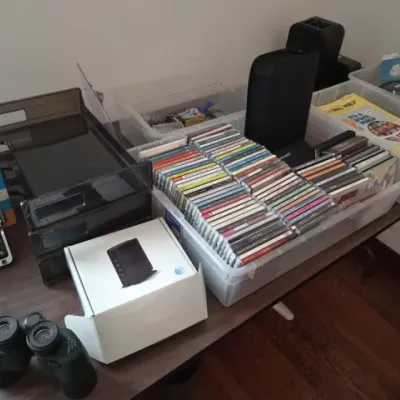 Sale Photo Thumbnail #139: Collection of home electronics and media, including a large lot of music CDs in plastic storage bins, AT&T cordless phones, boxed electronics, and a pair of binoculars.