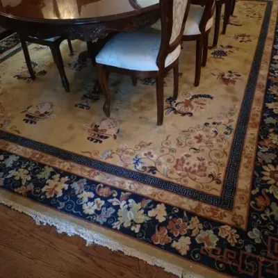 Sale Photo Thumbnail #40: Large vintage Chinese Art Deco wool area rug with a beige field, floral motifs, and a navy blue floral border, shown beneath a dark wood dining set.