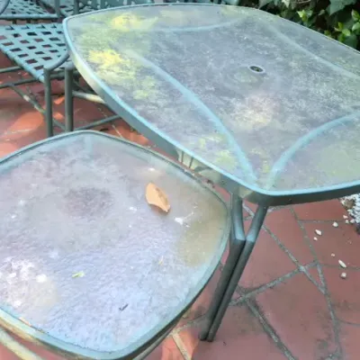 Sale Photo Thumbnail #176: Outdoor patio dining table with an umbrella hole and a matching side table, both featuring green metal frames and textured glass tops.