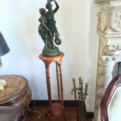 Sale Photo Thumbnail #18: Vintage figural mystery clock featuring two classical-style statues, set atop a tall wooden plant stand with barley-twist legs.