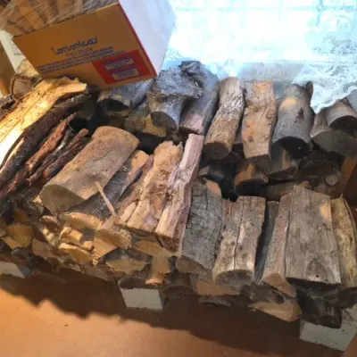 Sale Photo Thumbnail #158: Large stack of split firewood stored indoors on cinder blocks, accompanied by a cardboard box of additional kindling.