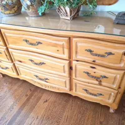 Sale Photo Thumbnail #50: French Provincial style knotty pine triple dresser with a glass top protector and ornate brass bail handles.