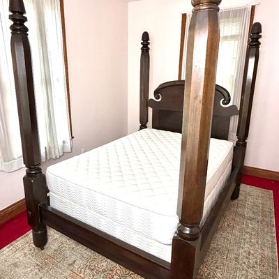 Traditional dark wood four-poster bed frame featuring octagonal posts, finial tops, and a scroll-cut headboard, shown with a mattress set.