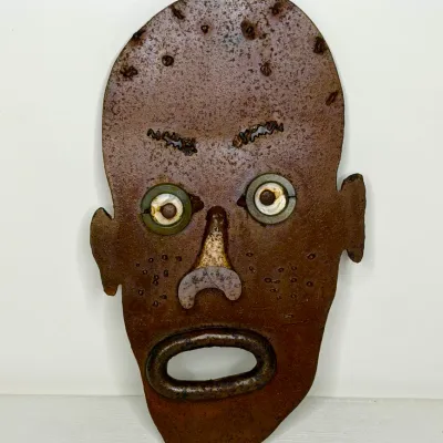 Rustic folk art scrap metal face mask sculpture with a heavily rusted finish.