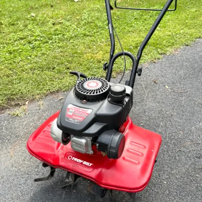 Troy-Bilt Ranger 140cc gas-powered front-tine garden tiller, featuring a red housing deck and black folding handlebars.