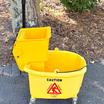 Yellow commercial mop bucket on casters, complete with attached side-press wringer and caution graphics.