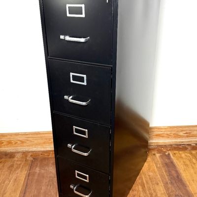 Black four-drawer metal filing cabinet with silver handles, label slots, and a key inserted in the top lock.