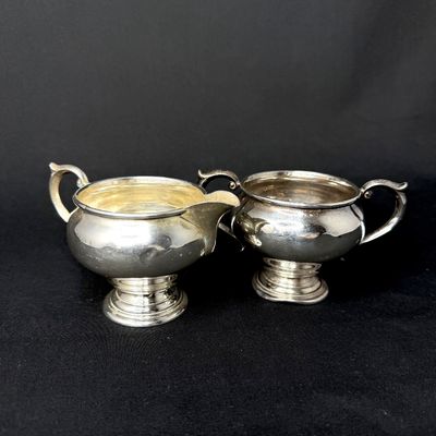 Vintage sterling silver or silver-plated creamer and open sugar bowl set with pedestal bases and scrolled handles.