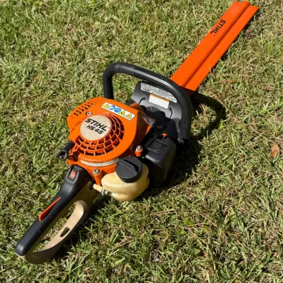 Stihl HS 45 gas-powered hedge trimmer with orange blade scabbard, showing typical signs of outdoor use.