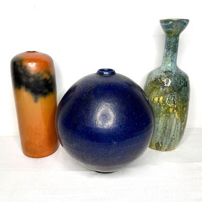 Trio of mid-century studio pottery vases in varied shapes and glazes, including an orange-and-black cylindrical piece, a large round...