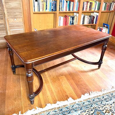 Traditional dark wood dining table featuring turned legs and a curved lower stretcher.