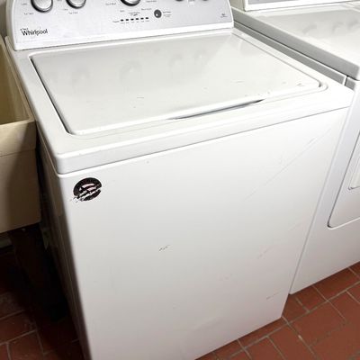 White top-loading Whirlpool washing machine with silver dial controls, showing light exterior scuffs and wear.