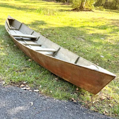 Vintage fiberglass-wrapped wooden pirogue canoe, featuring bench seating and a weathered finish.