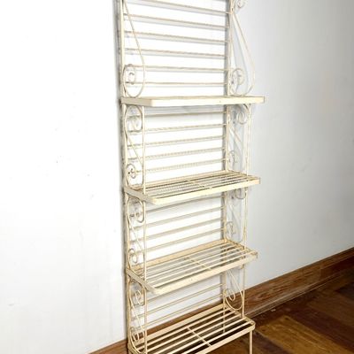 Vintage off-white wrought iron bakers rack featuring four slatted shelves and ornate scrollwork details.