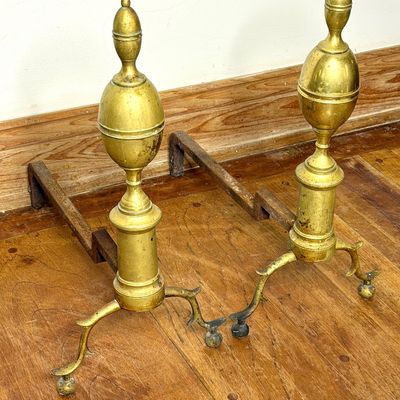 Pair of antique brass fireplace andirons featuring urn and finial tops with ornate spur legs and iron billet bars.