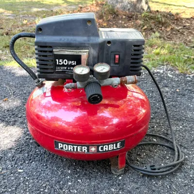 Porter-Cable 150 PSI pancake air compressor with attached gauges and power cord. Shows minor cosmetic wear and surface rust consistent...