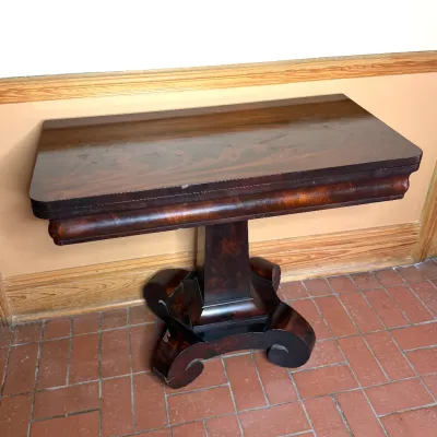 Antique Empire style mahogany card table featuring a fold-over top, Ogee apron, and scroll-footed pedestal base.
