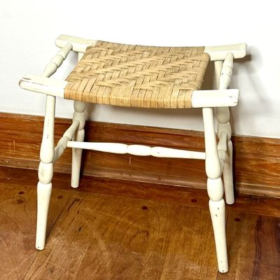Vintage white-painted wooden stool featuring turned spindle legs and a woven rush seat, showing light age-appropriate paint wear.
