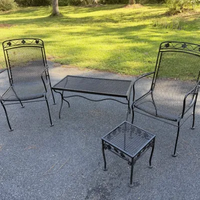 Four-piece black wrought iron patio set, featuring two armchairs with rose vine crests, a rectangular coffee table, and a small square...