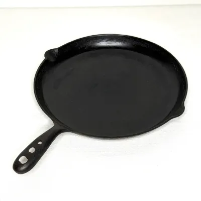 Vintage cast iron round griddle pan featuring a handle with multiple hanging holes and dual pour spouts.