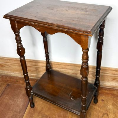 Vintage dark-stained wooden side table featuring turned spindle legs, a scalloped apron, and a lower display shelf. The wood finish shows...