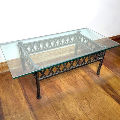 Modern wrought iron coffee table with a lattice apron base and a thick glass top.
