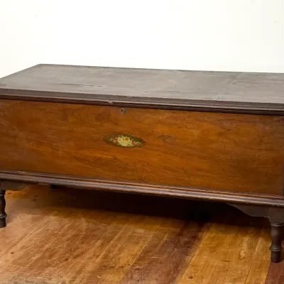 Vintage dark wood cedar chest with a central painted floral motif, keyhole detail, and turned legs.