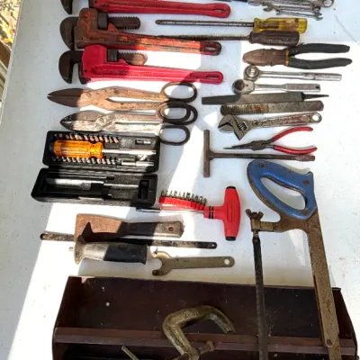 Assortment of vintage hand and power tools laid out on a table, including pipe wrenches, hacksaws, angle grinders, files, and a metal...