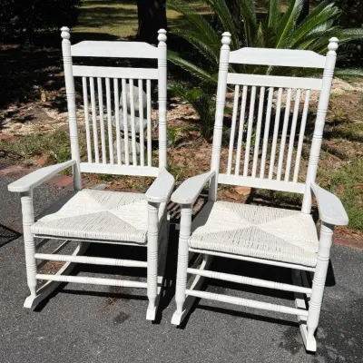 Pair of white painted wooden rocking chairs featuring slatted backs, turned posts, and woven rush seats.