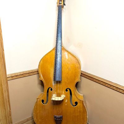 Vintage blonde upright double bass with dark wood fingerboard and tailpiece, showing light wear and finish patina.