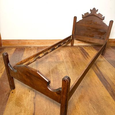 Antique wooden twin bed frame with carved crest headboard, footboard, and side rails.