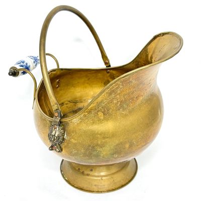 Vintage brass scuttle-style coal bucket with a lion head handle accent and a blue-and-white porcelain grip.