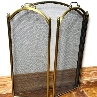 Vintage three-panel folding fireplace screen featuring a brass-tone arched frame, fine wire mesh, finials, and top handles.