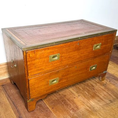 Vintage campaign-style wooden chest of drawers featuring a embossed leather insert top, brass recessed handles, and side bail carrying...