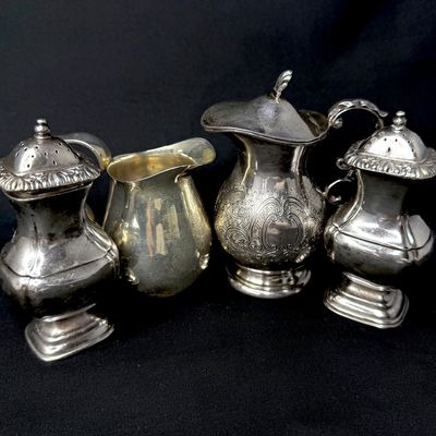 Four-piece collection of silver-plated tableware, including a pair of ornate salt and pepper shakers and two small cream pitchers,...