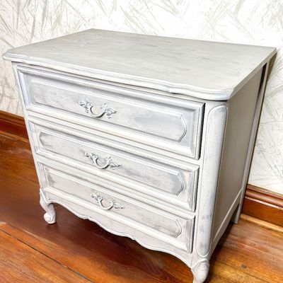 French Provincial style three-drawer nightstand or small chest, finished in painted gray distressed chalk paint with ornate silver pulls.