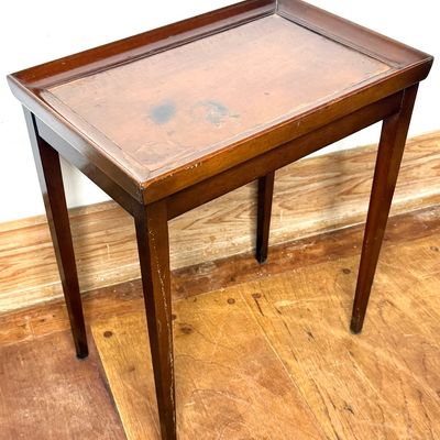 Vintage mahogany tray-top side table featuring a gallery edge and tapered legs. The top surface exhibits notable staining and wear to the...