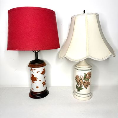 Two vintage ceramic table lamps with floral motifs, featuring one with a bold red drum shade and another with a cream scalloped fabric...