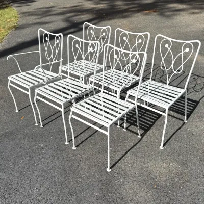 Set of six white wrought iron patio chairs featuring decorative loop backs and slatted seats, including one armchair.
