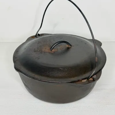 Vintage cast iron Dutch oven with lid and wire bail handle, featuring minor surface rust.